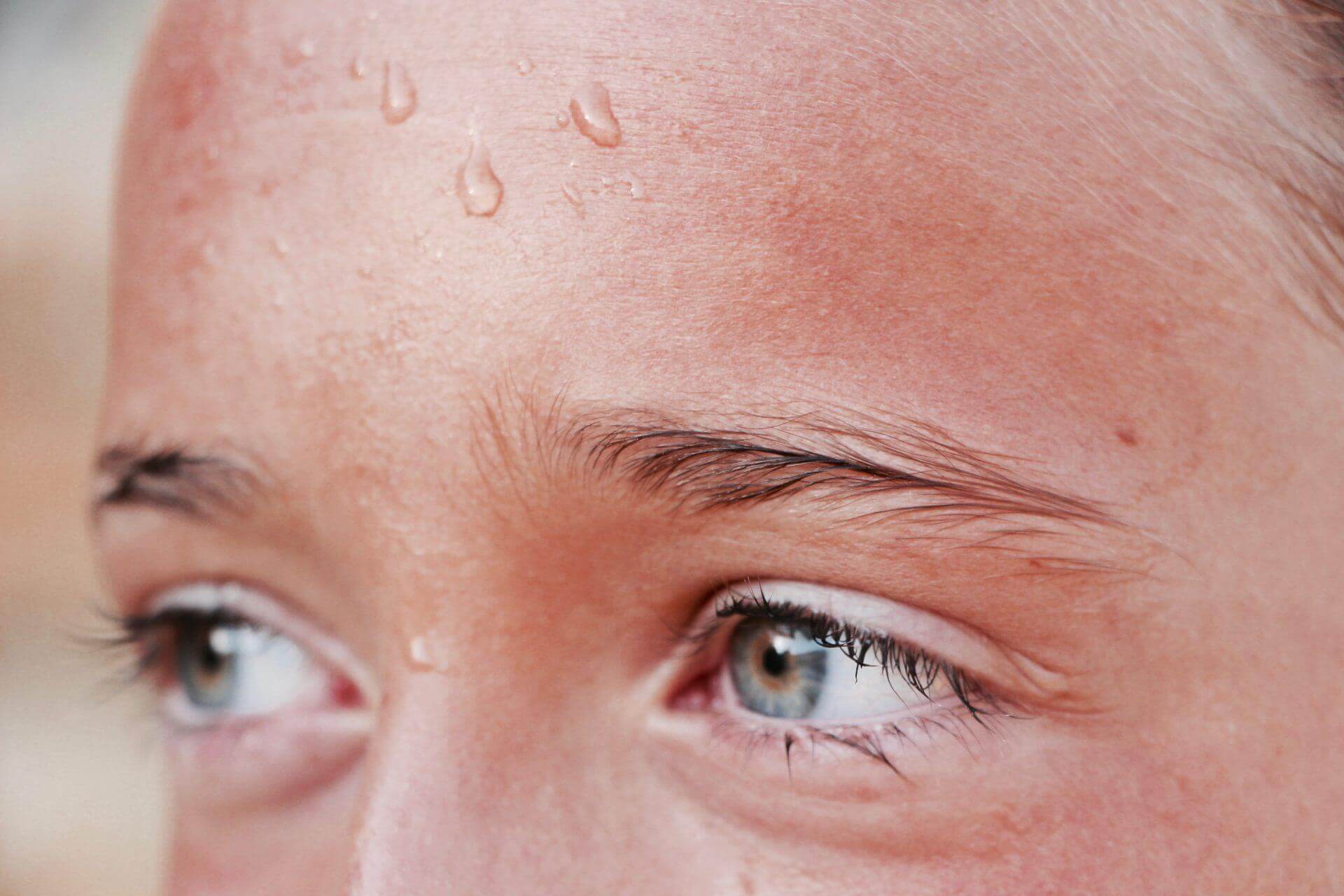 A close up of a person's blue/green eyes with sweat running down their forehead.