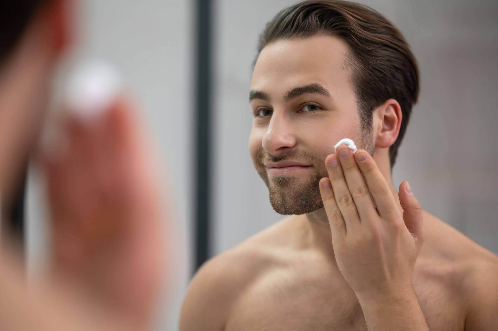 Man standing near mirror applying skincare cream to his face